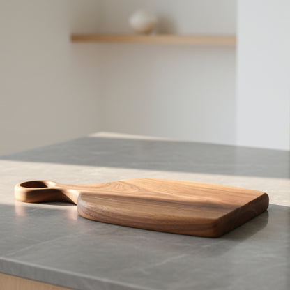 Black walnut wooden chopping board on a gray marble kitchen countertop with a neutral background. Warm and earthy design, irregular shape. Minimalist Scandinavian style. 