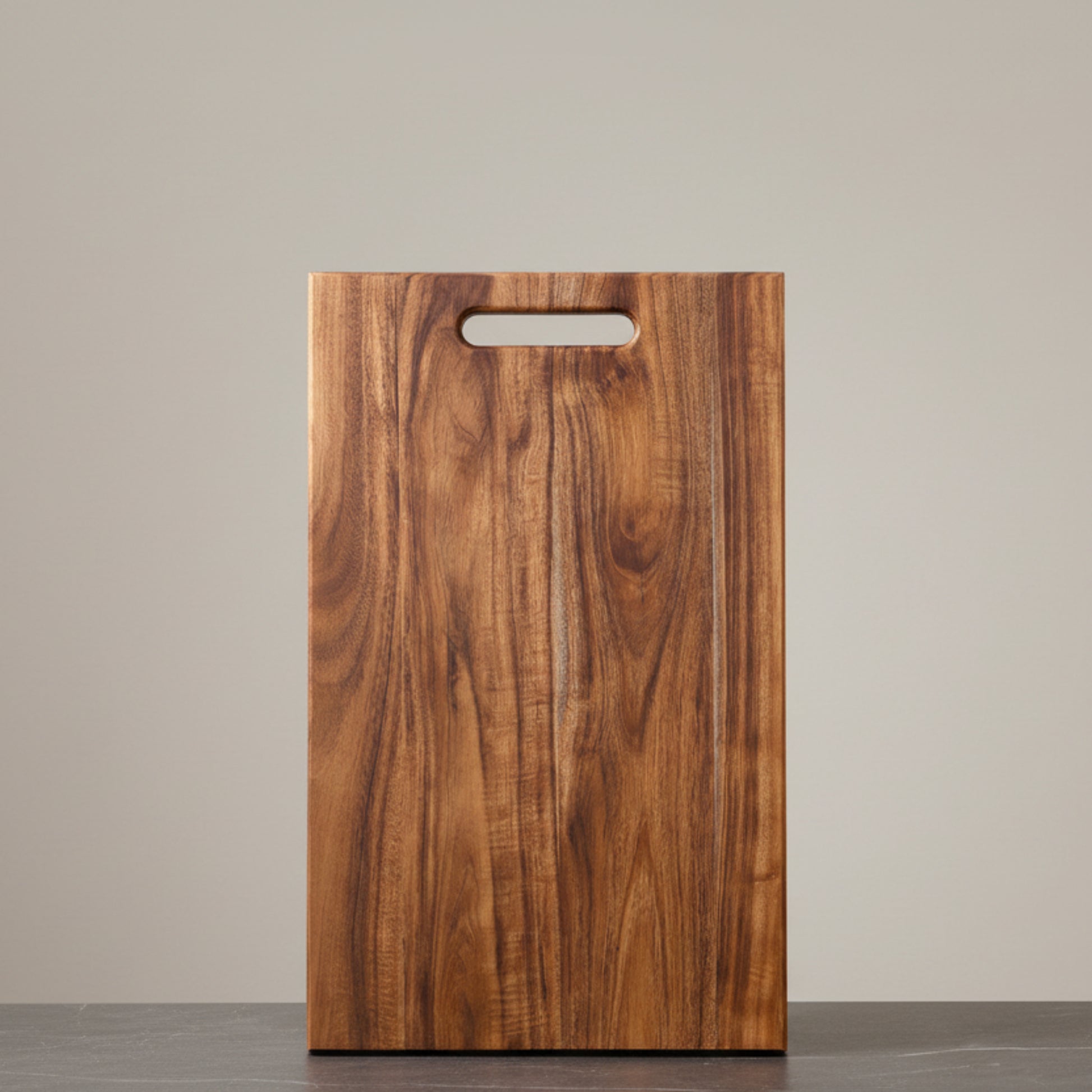 Wooden acacia mangium cutting board with a handle on a neutral background and on a dark grey marble surface. Earthy, warm and natural ambience. 