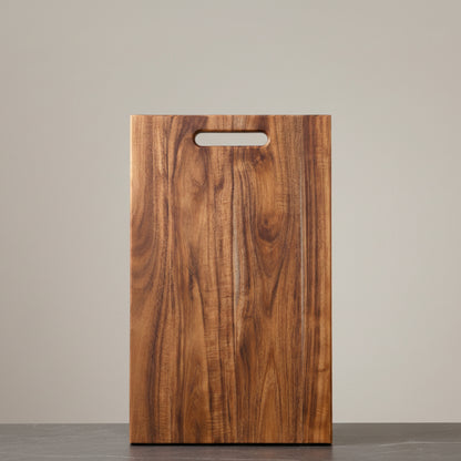 Wooden acacia mangium cutting board with a handle on a neutral background and on a dark grey marble surface. Earthy, warm and natural ambience. 