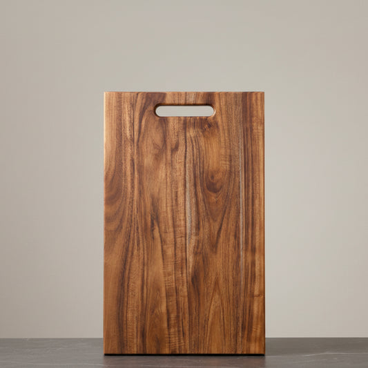 Wooden acacia mangium cutting board with a handle on a neutral background and on a dark grey marble surface. Earthy, warm and natural ambience. 