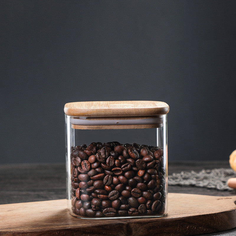 A small kitchen jar with wooden lid filled with coffee beans on a wooden kitchen surface on a dark grey background. A warm minimalist interior with simple decor and simple design. Storage kitchen jar. 
