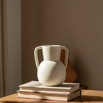Beige Scandinavian decor inspired ceramic binaural vase on two books and a table. Warm tones. Minimalist interiors.