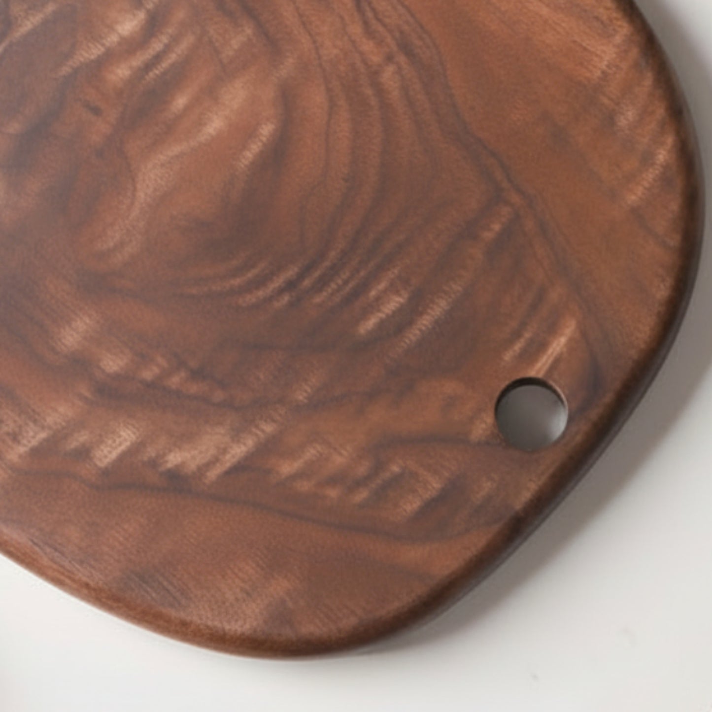 Black walnut wooden chopping board close up on a neutral white background. Warm and earthy design, irregular shape. Minimalist Scandinavian style. 