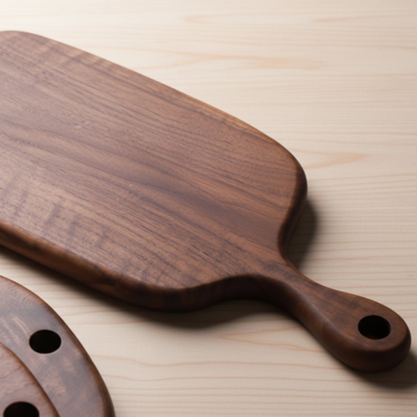 Black walnut wooden chopping board with handle on a light wooden surface. Warm and earthy design, irregular shape. Minimalist Scandinavian style. 
