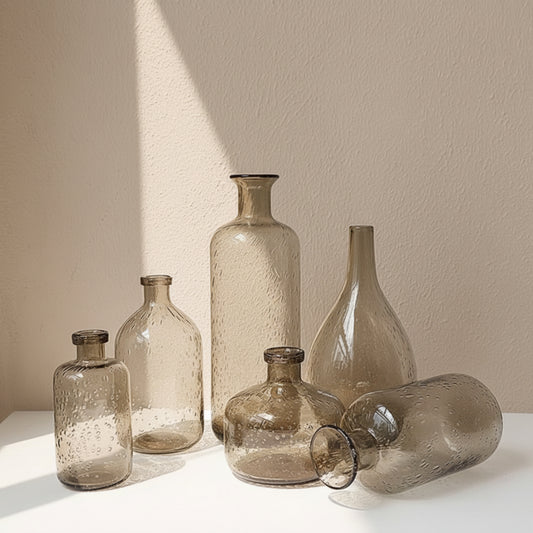 Set of glass bottles in different forms and sizes on a white surface with a neutral beige background. 