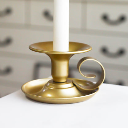Gold candle holder with a white candle on a blurred background on a white surface. Minimalist design. Elegant, modern and antique. 