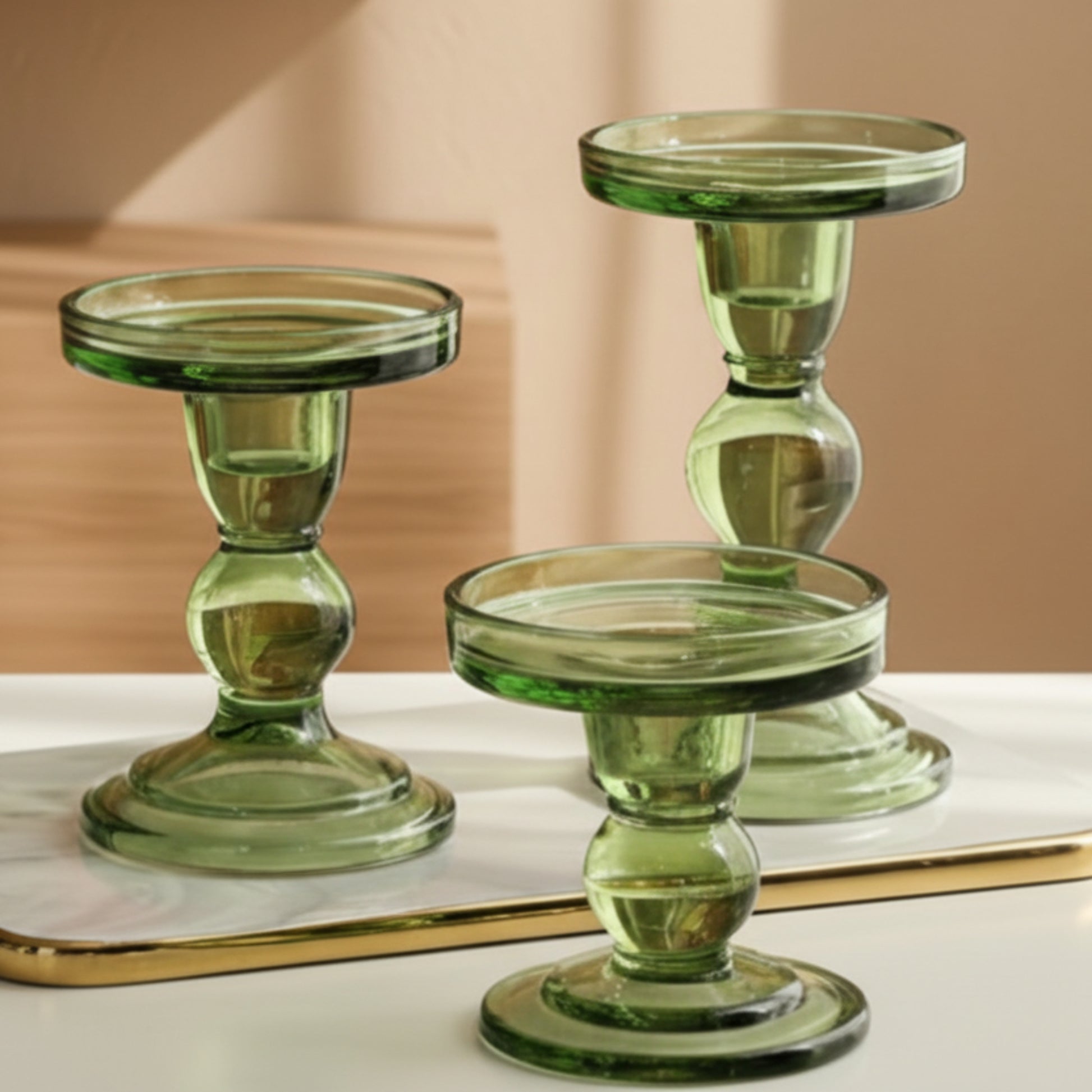 Three green glass candle holders on a bright surface with a beige-brown background. Warm and earthy home decor and atmosphere. 