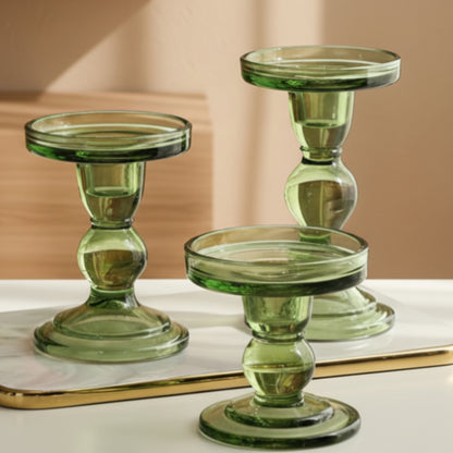 Three green glass candle holders on a bright surface with a beige-brown background. Warm and earthy home decor and atmosphere. 