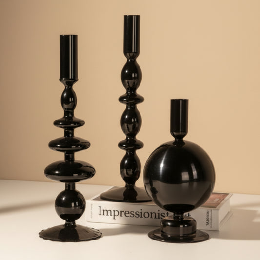 Set of three black decorative candle holders on a white surface with a book and on a beige warm background. 
Scandinavian inspired minimalist decor design. Sleek and modern decor. 
