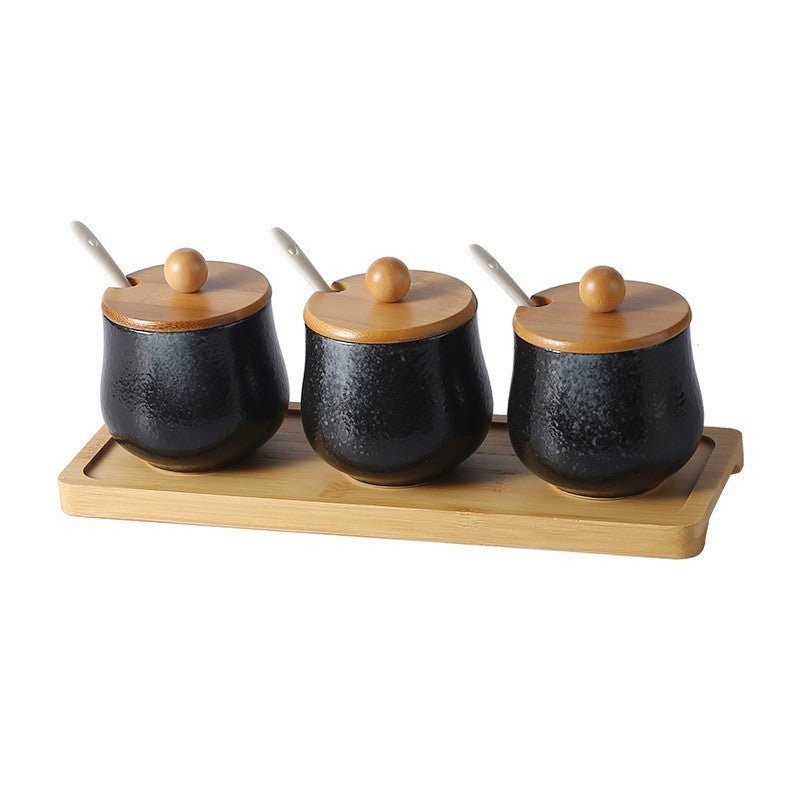 A set of three ceramic jars with Japanese style designs, featuring a speckled black and white pattern on a white background. The jars come with wooden lids and are displayed on a wooden tray.
