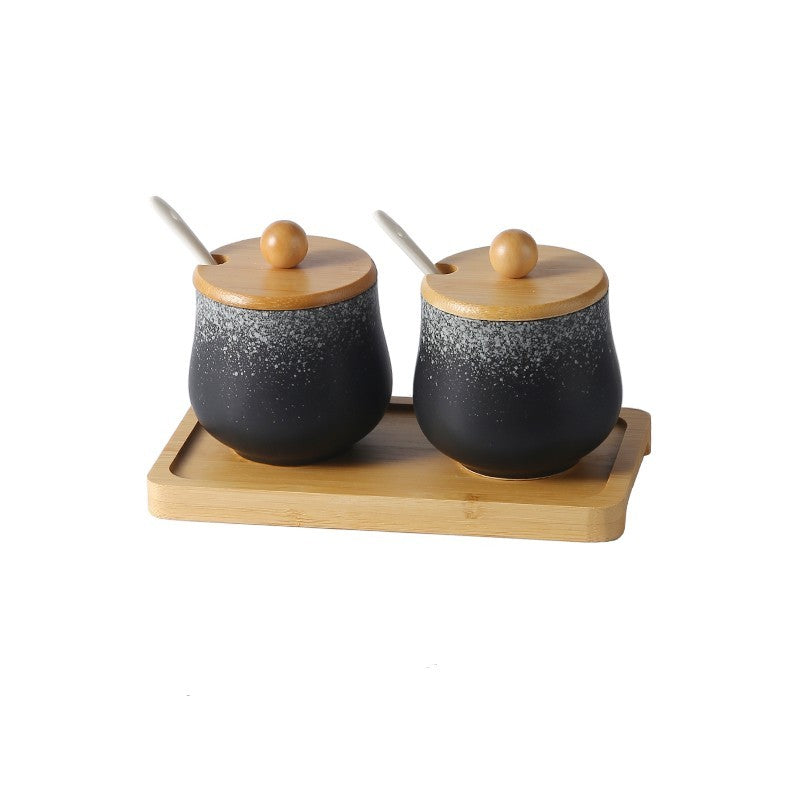 A set of two ceramic jars with Japanese style designs, featuring a speckled black and white pattern on a white background. The jars come with wooden lids and are displayed on a wooden tray.