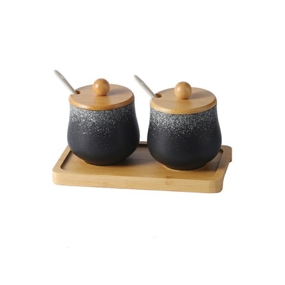 A set of two ceramic jars with Japanese style designs, featuring a speckled black and white pattern on a white background. The jars come with wooden lids and are displayed on a wooden tray.