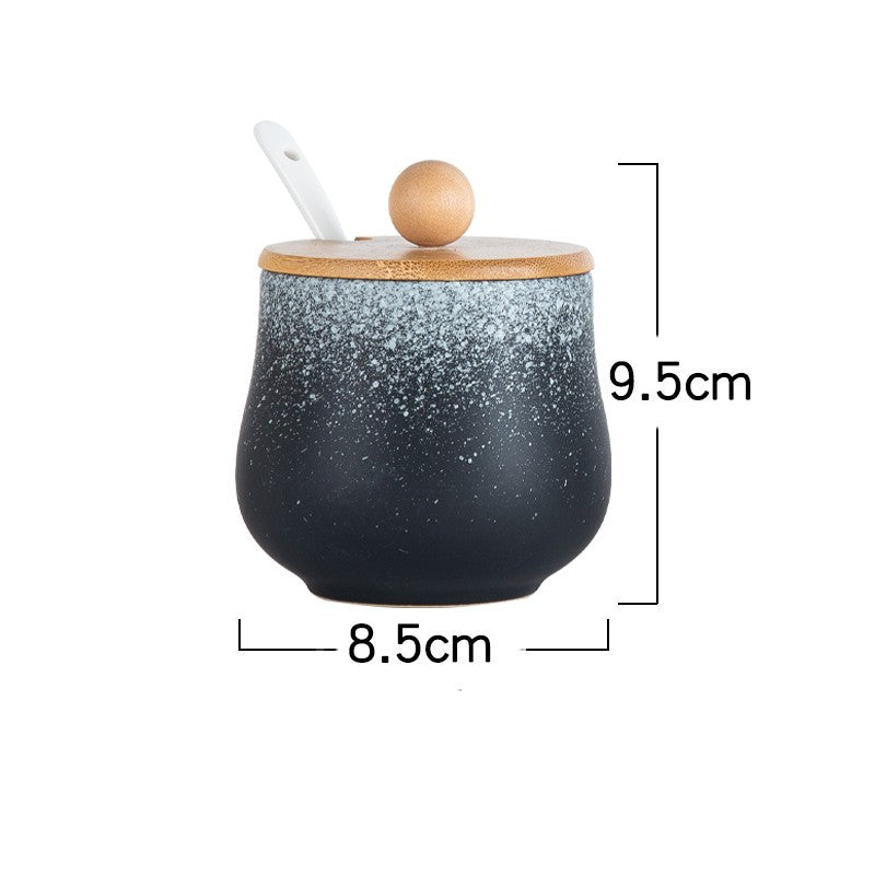 A ceramic jar with Japanese style designs, featuring a speckled black and white pattern on a white background and with measurements. The jars comes with a wooden lid and a spoon.
