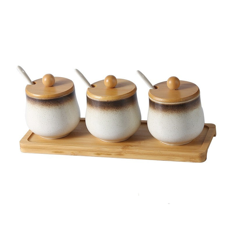 A set of three ceramic jars with Japanese style designs, featuring a speckled brown and white pattern on a white background. The jars come with wooden lids and are displayed on a wooden tray.