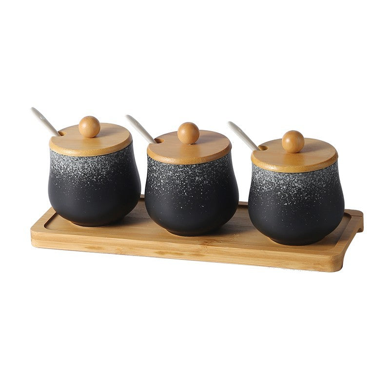 A set of three ceramic jars with Japanese style designs, featuring a speckled black and white pattern on a white background. The jars come with wooden lids and are displayed on a wooden tray.