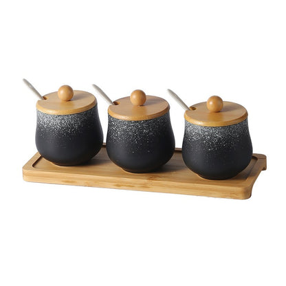 A set of three ceramic jars with Japanese style designs, featuring a speckled black and white pattern on a white background. The jars come with wooden lids and are displayed on a wooden tray.
