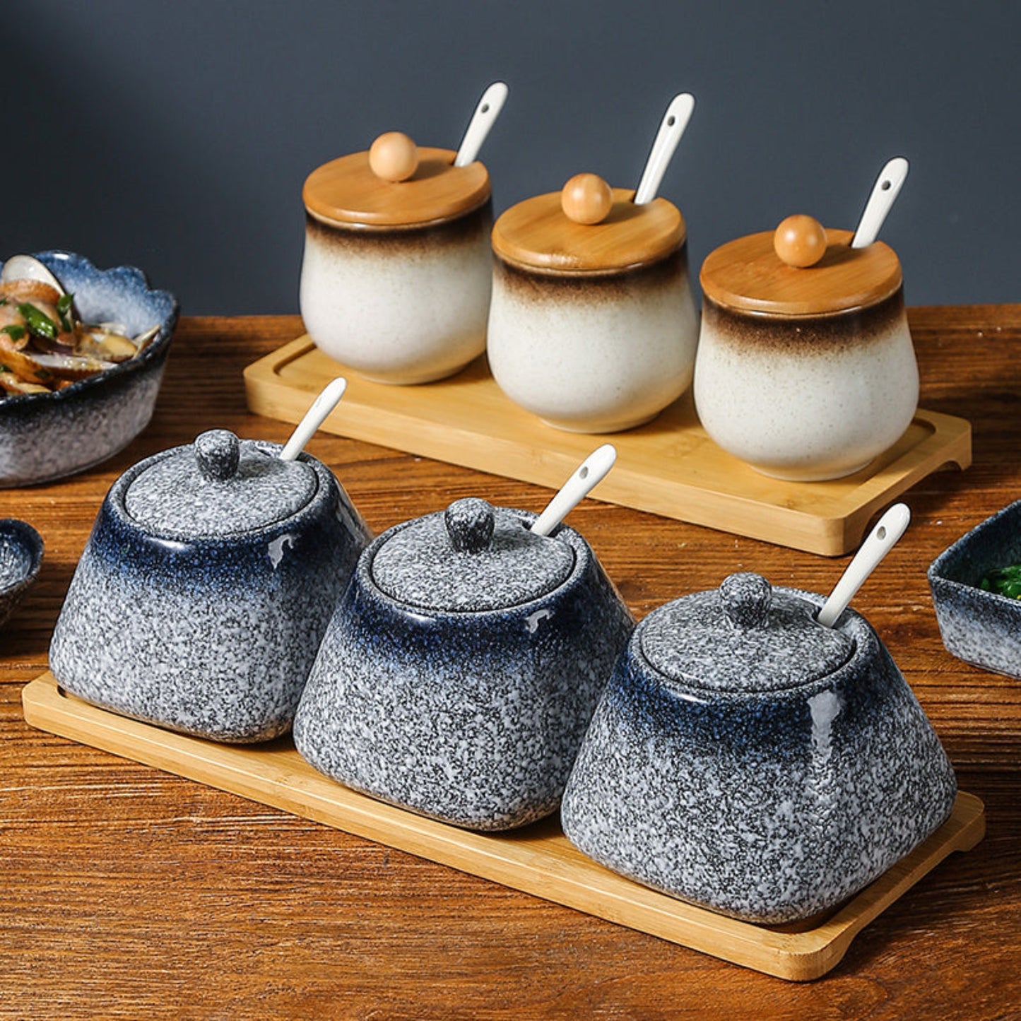 Set of blue and white ceramic containers with wooden lids (only white jars) and spoons on a wooden tray. 