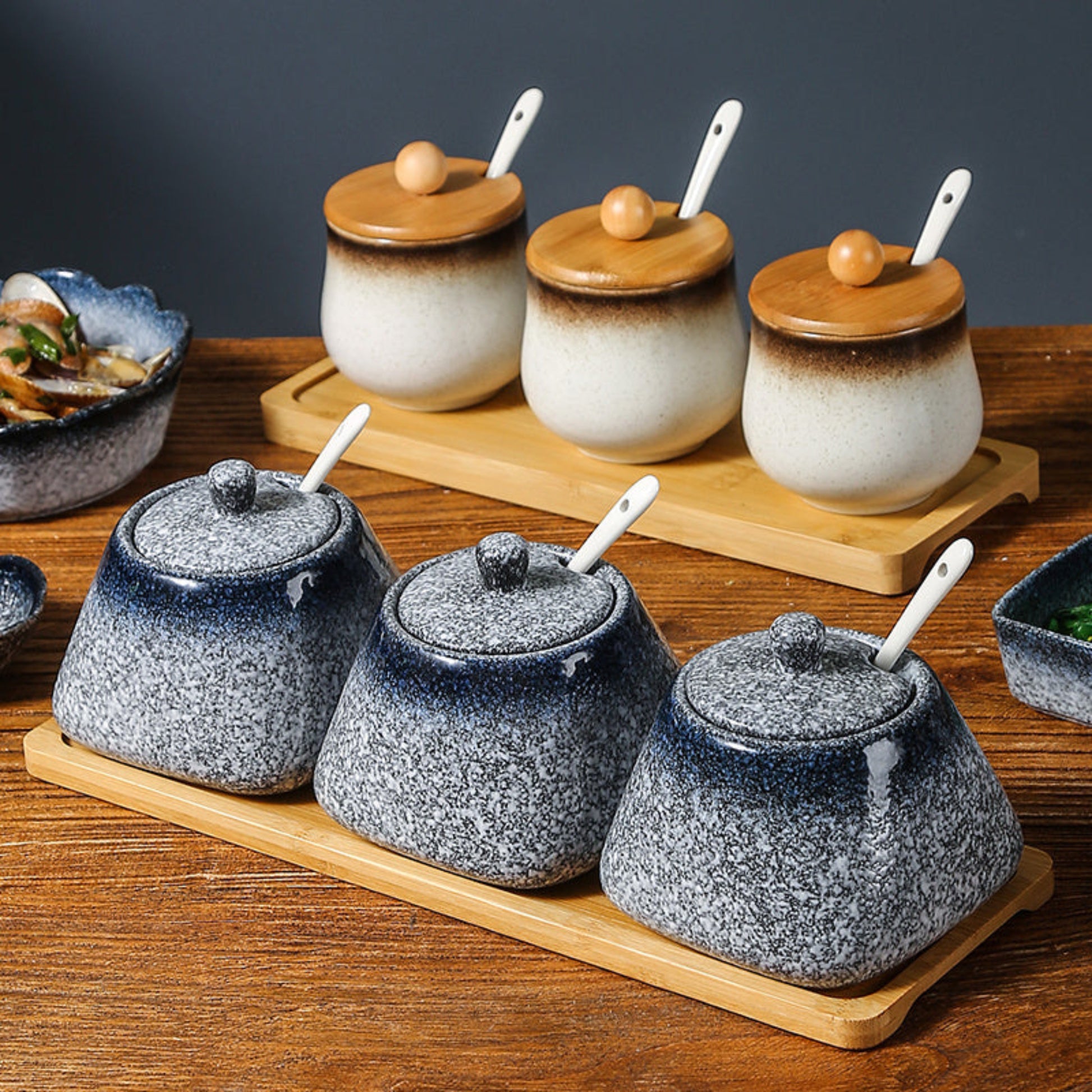 Set of blue and white ceramic containers with wooden lids (only white jars) and spoons on a wooden tray. 