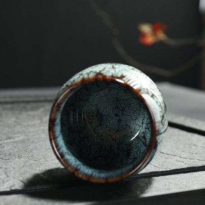 Ceramic cup with unique glaze pattern on a textured dark surface. Natural and earthy ambience. 