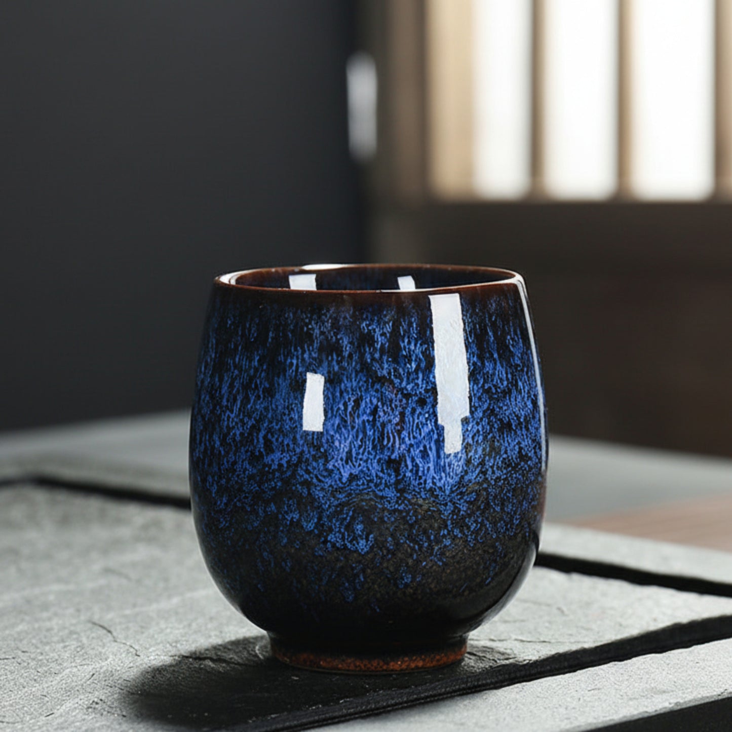 Ocean blue ceramic cup with unique glaze pattern on a textured surface and a blurred background. Natural and earthy ambience. 