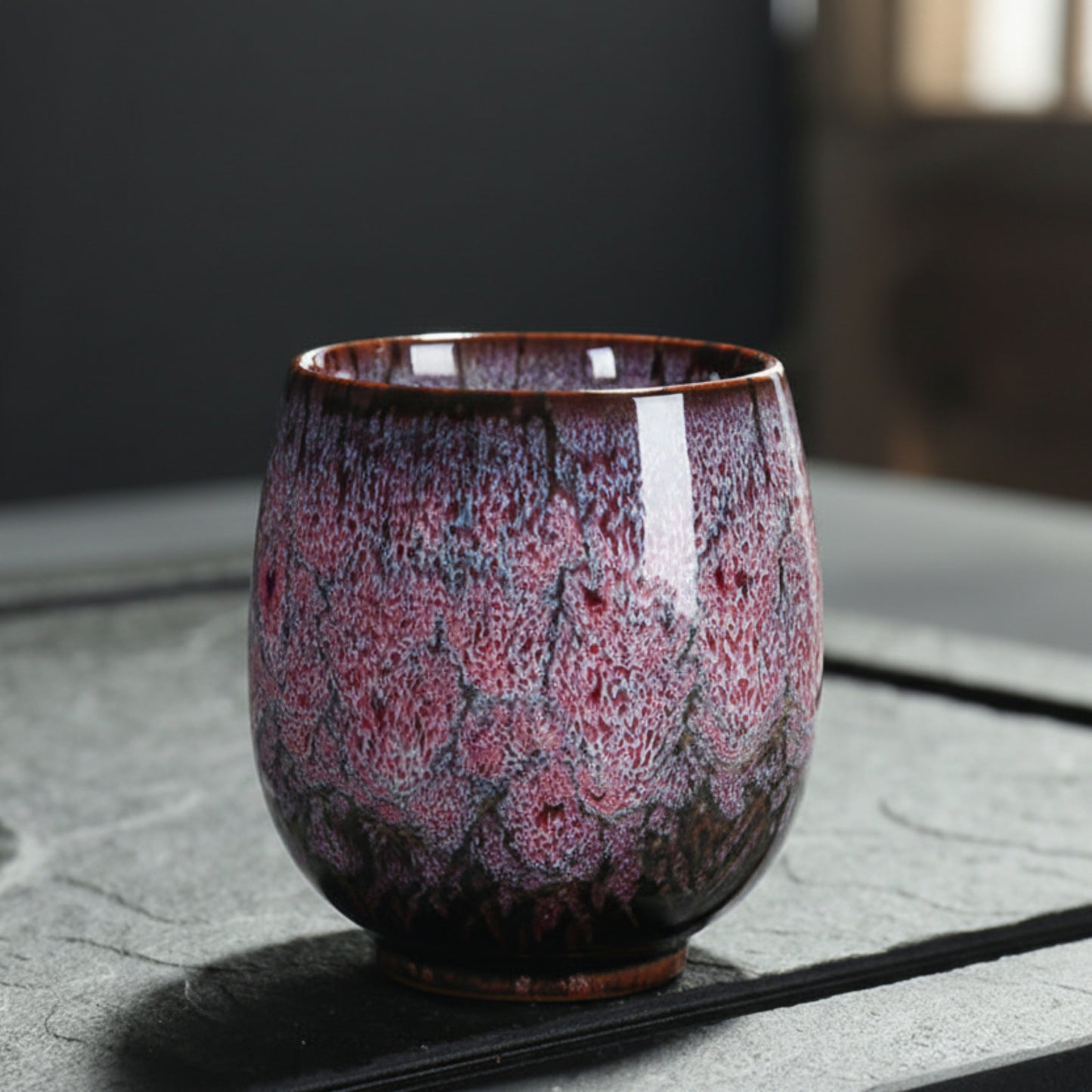 Purple and brown ceramic cup with unique glaze pattern on a textured surface and a blurred background. Natural and earthy ambience. 