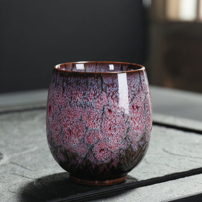 Purple and brown ceramic cup with unique glaze pattern on a textured surface and a blurred background. Natural and earthy ambience. 