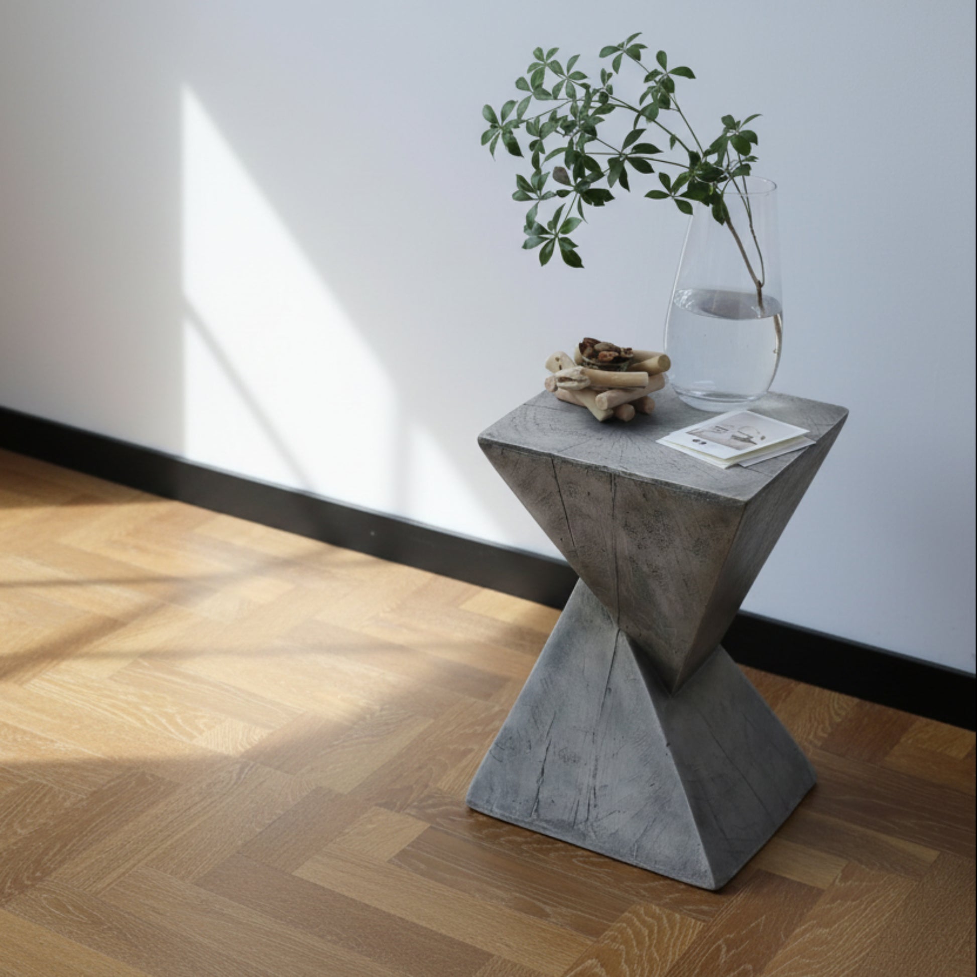 Minimalist grey side table on a white background on a wooden floor.  Decor piece and flower on top. Modern decor piece. Clean lines, natural materials, and timeless piece. 