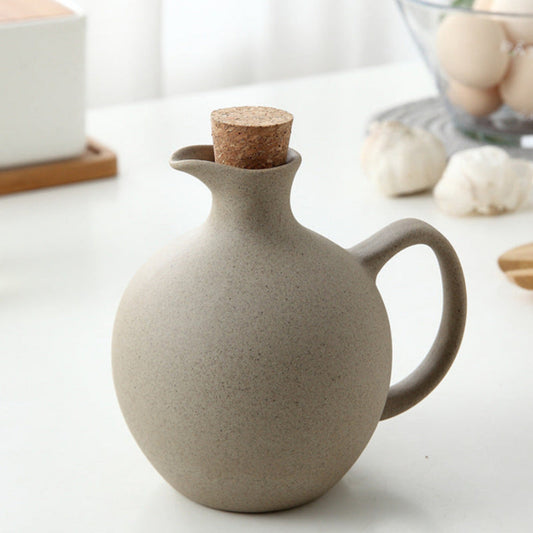 Beige ceramic oil dispenser with cork lid on a light surface. Earthy kitchen and home decor with natural textures and warm tones. 