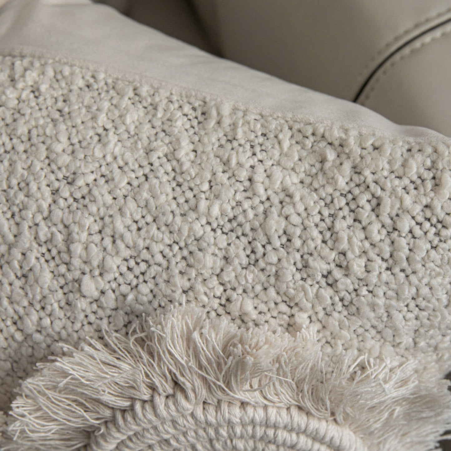 Close-up of a textured beige pillow with fringe on a blurred background. Cotton linen pillowcase on a beige sofa. Stylish pillowcase. Modern accessories, natural material. 
