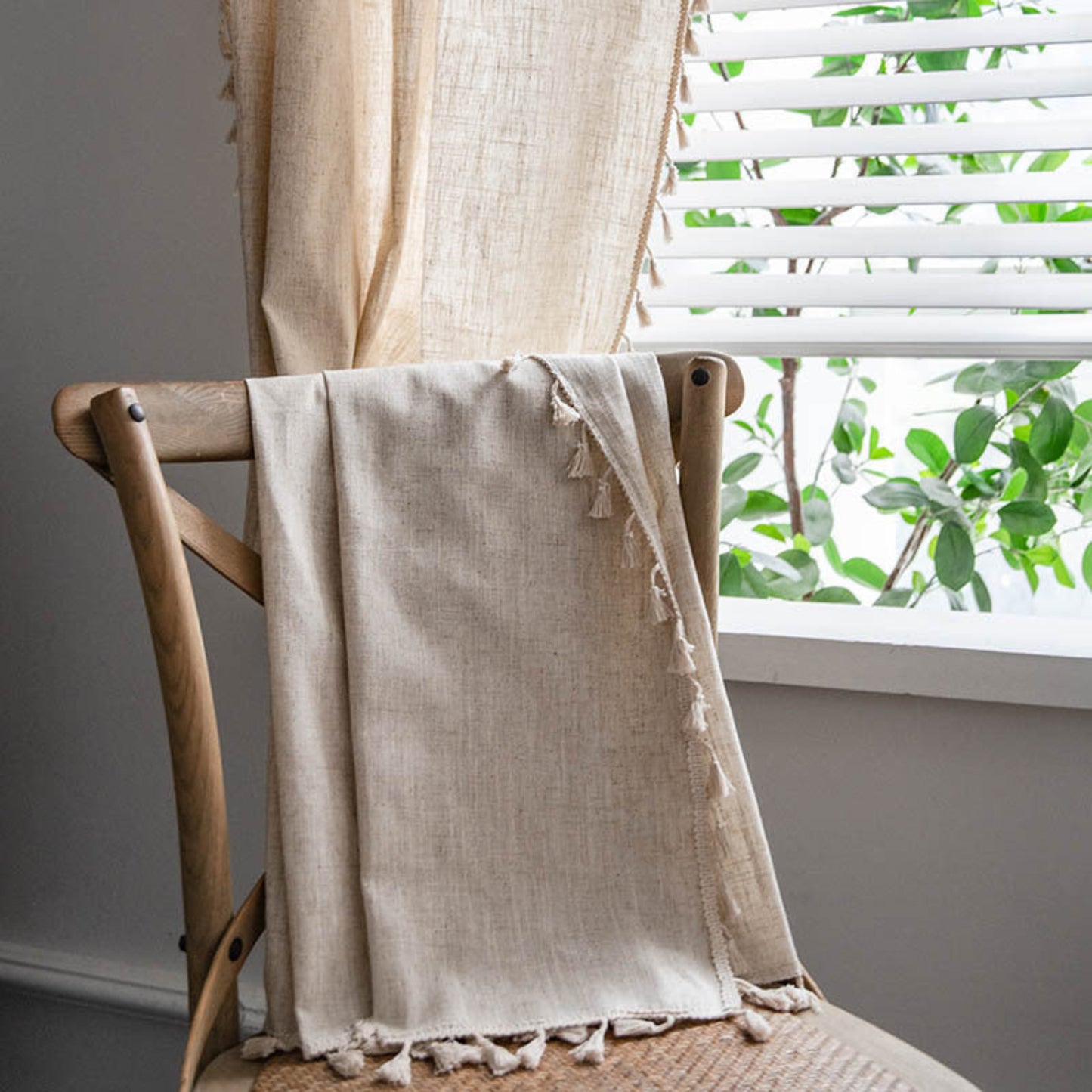 Curtain over a wooden chair in front of a window. Natural decor styling curtain for calm and modern interiors. warm and pure. Minimalist and earthy curtain.