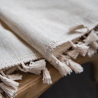 Close-up of a beige curtain with tassels on a wooden surface. Natural decor styling curtain for calm and modern interiors.