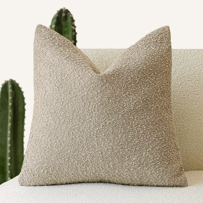 A beige Decorative Boucle Pillow Cover with a textured surface displayed on a neutral background and a cactus in the background. Warm and cozy decor ambience. 