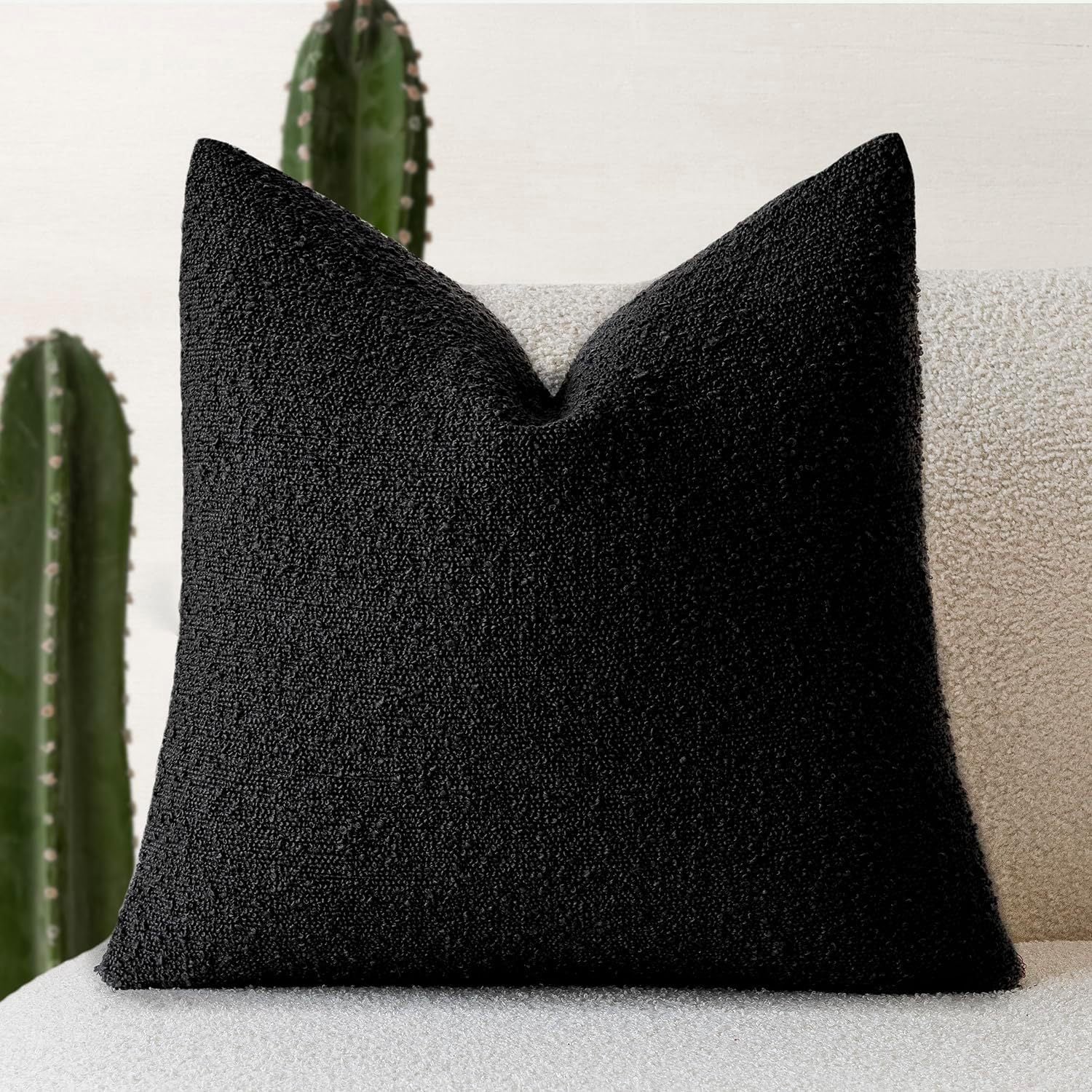 A black Decorative Boucle Pillow Cover with a textured surface displayed on a neutral background and a cactus in the background. Warm and cozy decor ambience. 