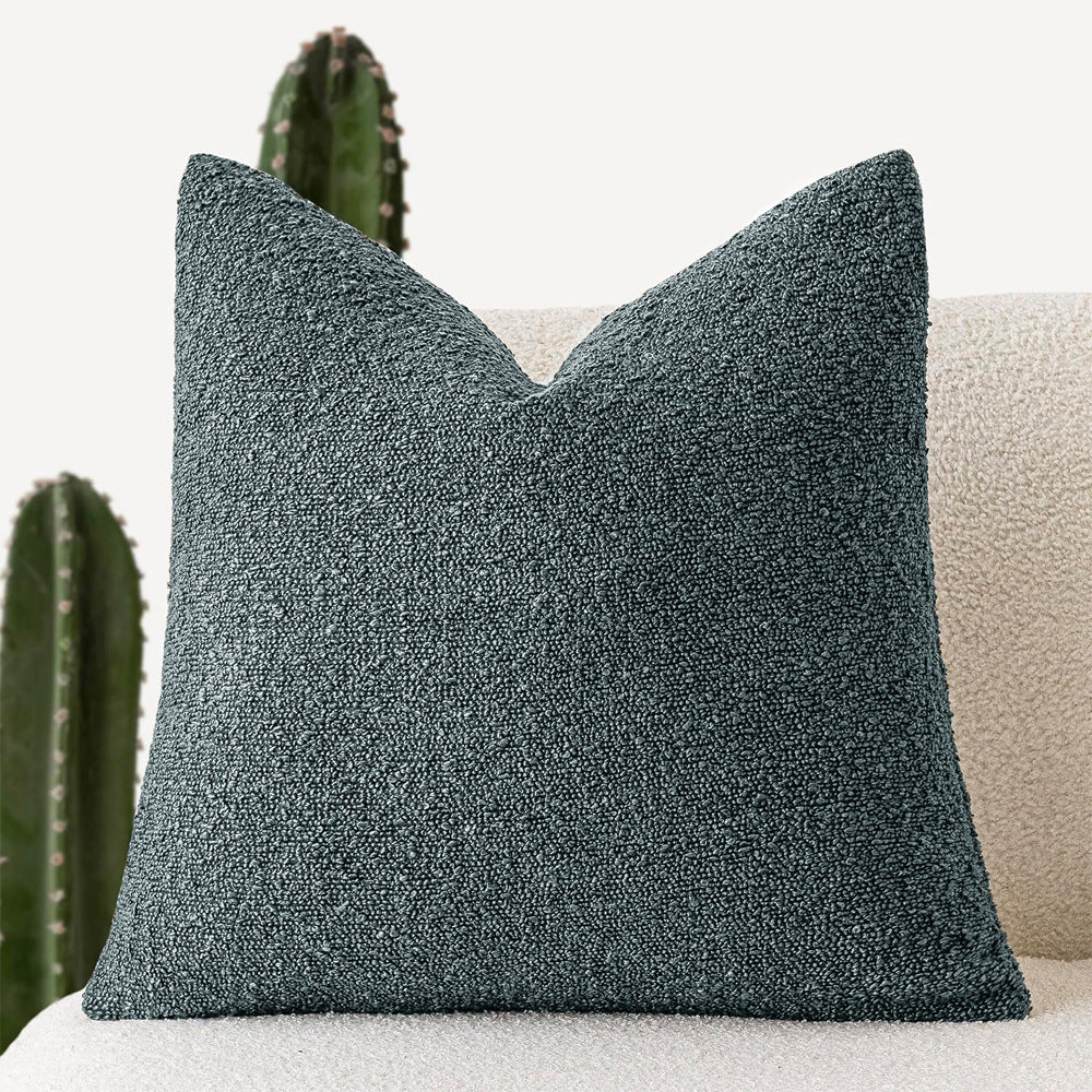 A blue-gray Decorative Boucle Pillow Cover with a textured surface displayed on a neutral background and a cactus in the background. Warm and cozy decor ambience. 