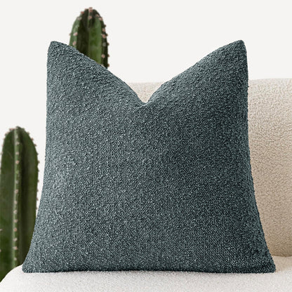 A blue-gray Decorative Boucle Pillow Cover with a textured surface displayed on a neutral background and a cactus in the background. Warm and cozy decor ambience. 