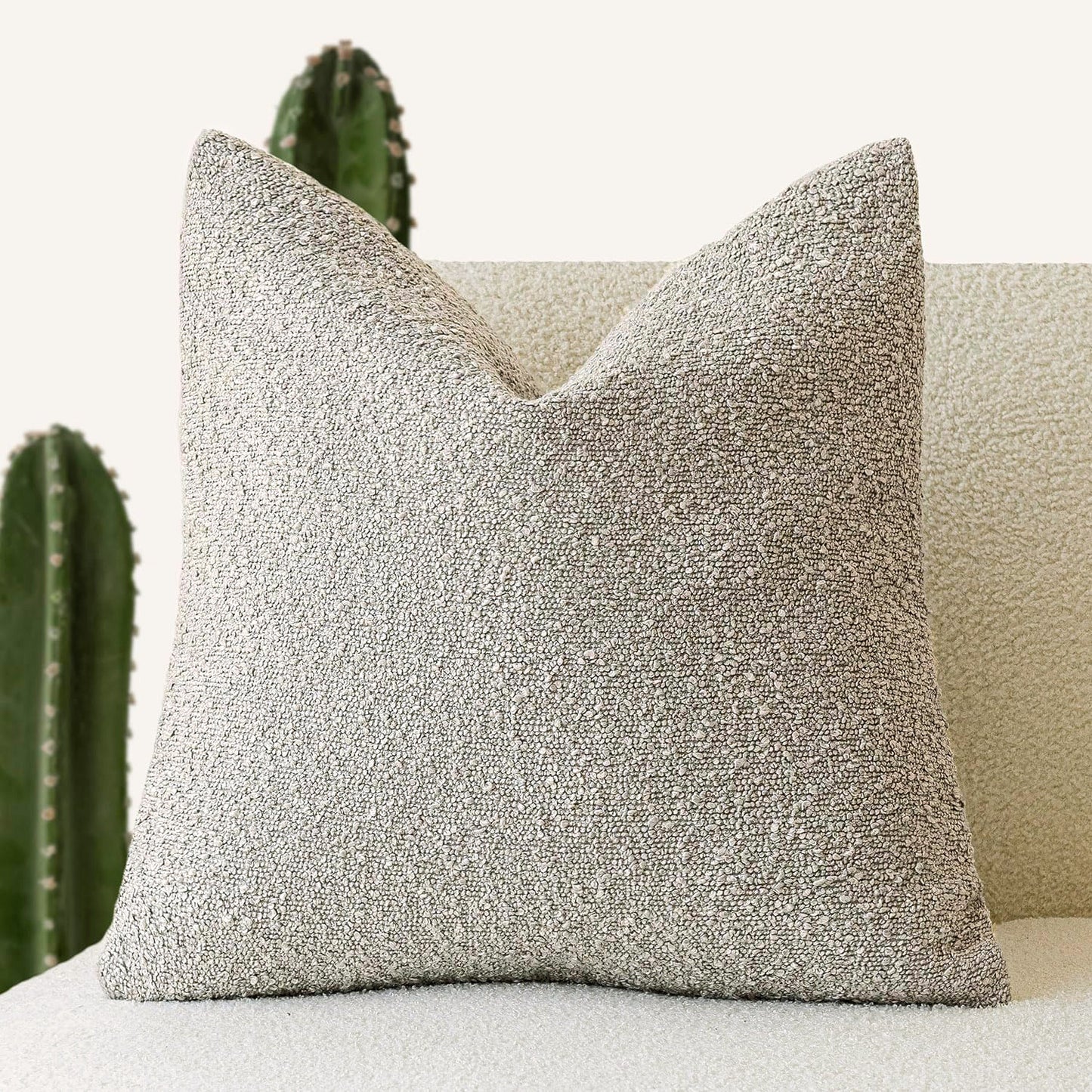 A deep beige Decorative Boucle Pillow Cover with a textured surface displayed on a neutral background and a cactus in the background. Warm and cozy decor ambience. 