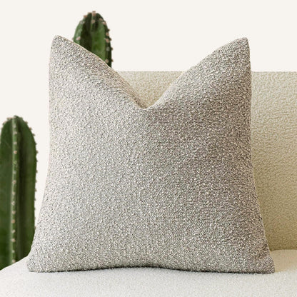 A deep beige Decorative Boucle Pillow Cover with a textured surface displayed on a neutral background and a cactus in the background. Warm and cozy decor ambience. 