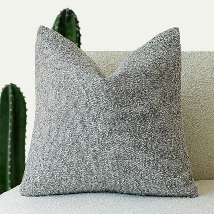 A gray Decorative Boucle Pillow Cover with a textured surface displayed on a neutral background and a cactus in the background. Warm and cozy decor ambience. 