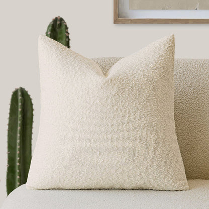 A light beige Decorative Boucle Pillow Cover with a textured surface displayed on a neutral background and a cactus in the background. Warm and cozy decor ambience. 