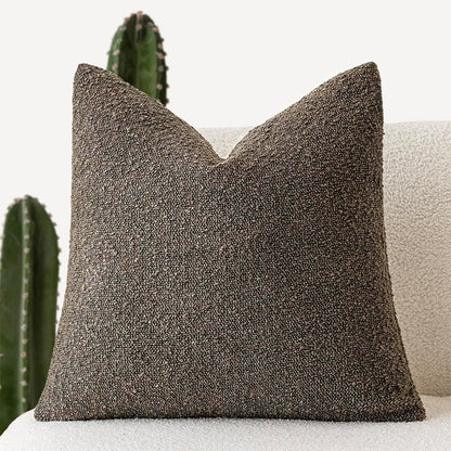 A light gray Decorative Boucle Pillow Cover with a textured surface displayed on a neutral background and a cactus in the background. Warm and cozy decor ambience. 