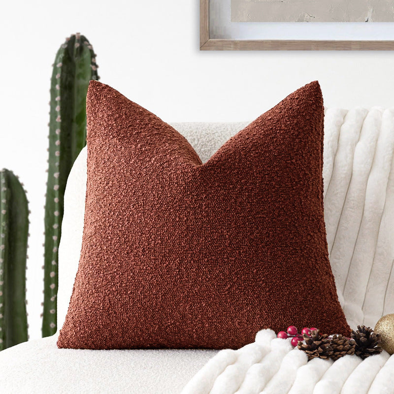 A red Decorative Boucle Pillow Cover with a textured surface displayed on a neutral background and a cactus in the background. Warm and cozy decor ambience. 