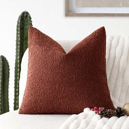 A red Decorative Boucle Pillow Cover with a textured surface displayed on a neutral background and a cactus in the background. Warm and cozy decor ambience. 