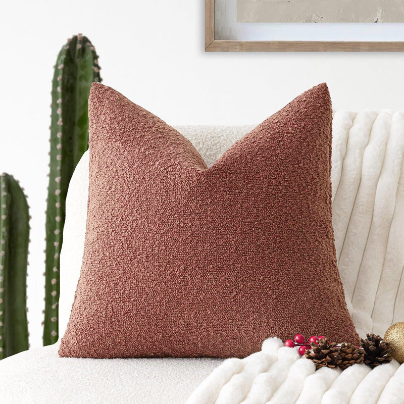 A wine red Decorative Boucle Pillow Cover with a textured surface displayed on a neutral background and a cactus in the background. Warm and cozy decor ambience. 