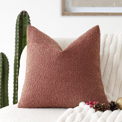A wine red Decorative Boucle Pillow Cover with a textured surface displayed on a neutral background and a cactus in the background. Warm and cozy decor ambience. 