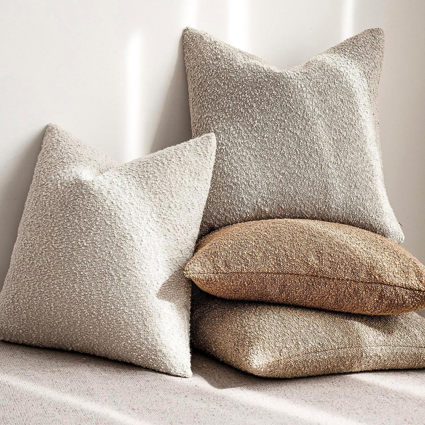 Four textured boucle pillows in beige, brown, and gray on a natural background. Warm and cozy decor ambience. 