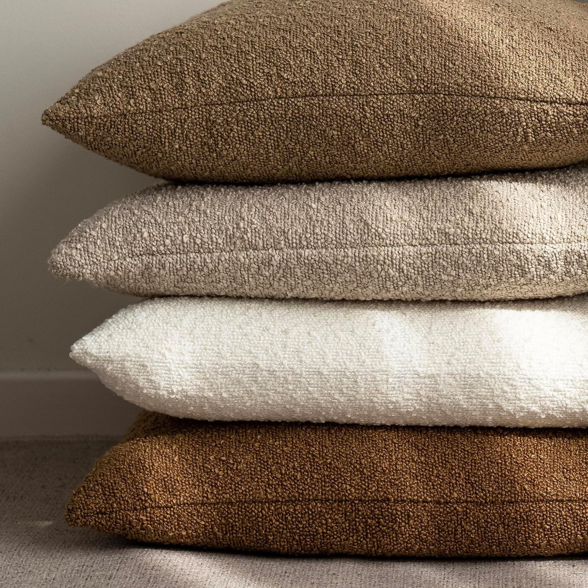 Stack of white, brown and beige textured boucle pillows on a natural background. Warm and cozy decor ambience. 