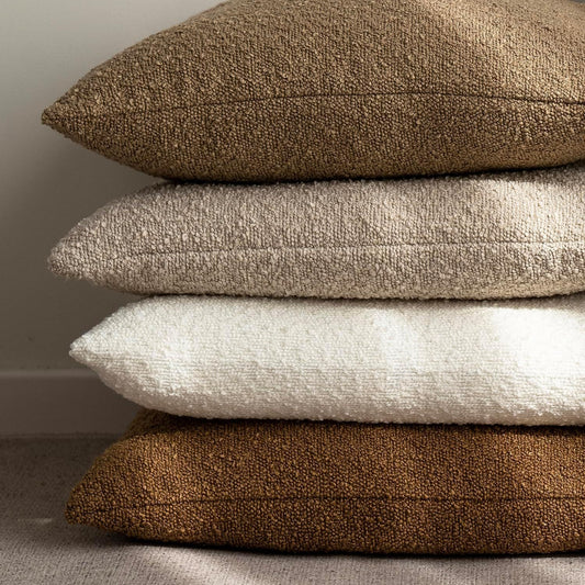 Stack of white, brown and beige textured boucle pillows on a natural background. Warm and cozy decor ambience. 