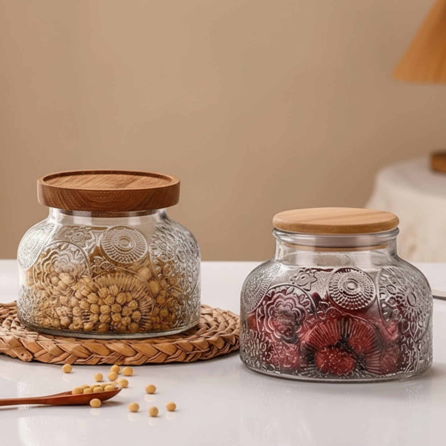 Two glass jars with wooden and bamboo lids on a table, one filled with seeds and the other with dried fruits.