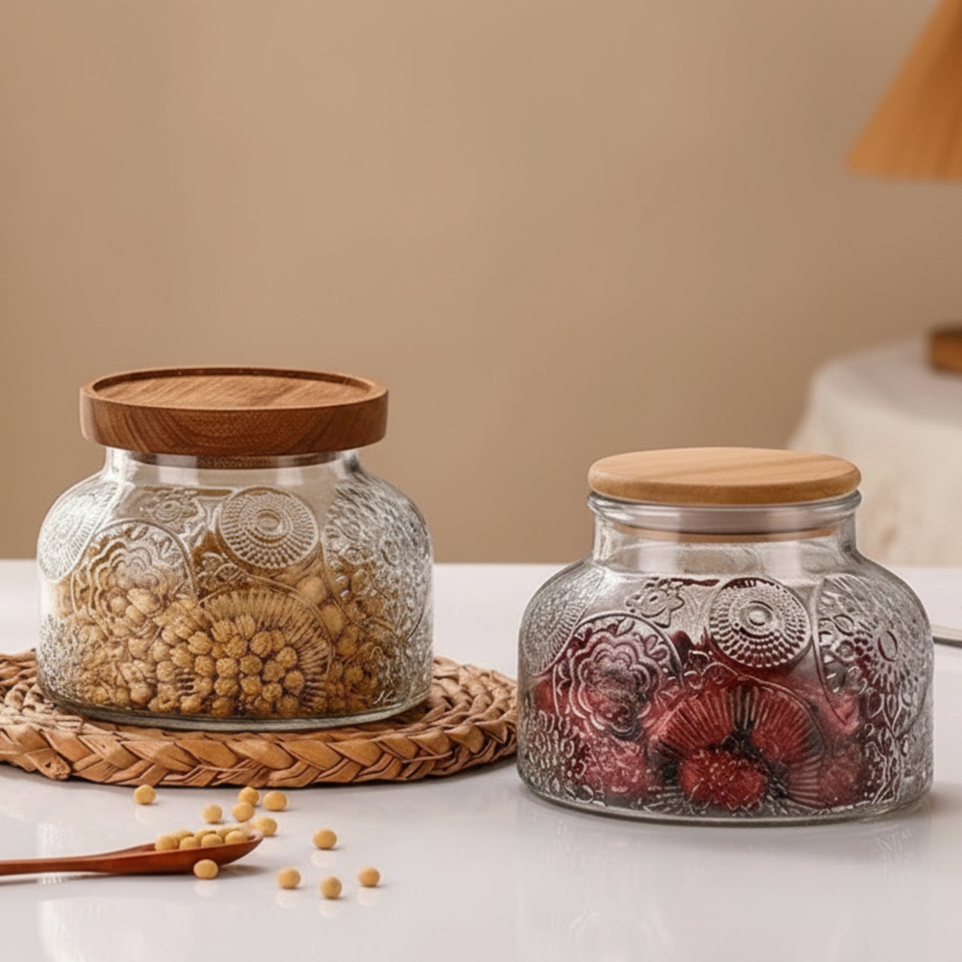 Two glass jars with wooden and bamboo lids on a table, one filled with seeds and the other with dried fruits.