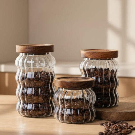 Three glass jars with wooden lids filled with coffee beans on a light surface on a wooden table. Scandinavian kitchen decor inspired. Simplicity, natural materials, and warm tones in the background. 